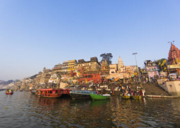 A scenic view of Varanasi’s ghats from the Ganges River at sunrise, showcasing temples, boats, and the spiritual essence of the city.