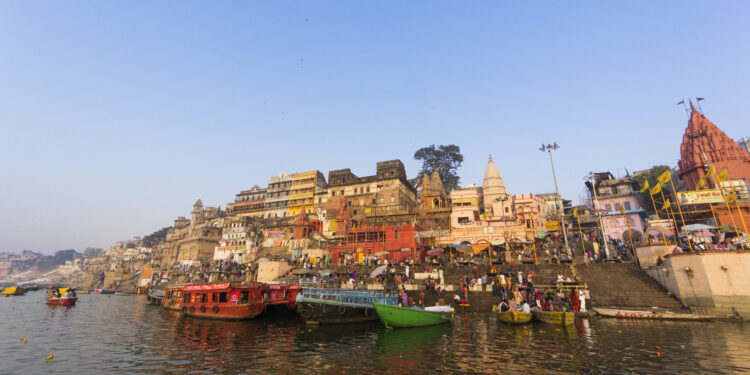 A scenic view of Varanasi’s ghats from the Ganges River at sunrise, showcasing temples, boats, and the spiritual essence of the city.