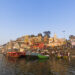 A scenic view of Varanasi’s ghats from the Ganges River at sunrise, showcasing temples, boats, and the spiritual essence of the city.