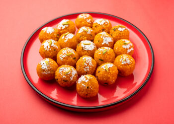 Boondi laddoos prasad decorated with silver leaf and pistachios, served on a red plate for Hanuman Jayanti