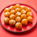 Boondi laddoos prasad decorated with silver leaf and pistachios, served on a red plate for Hanuman Jayanti