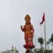 Statue of Lord Hanuman standing with a raised hand and mace, adorned with gold ornaments and red flags, at a Hindu temple