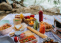 Colourful picnic spread on a blanket with fresh food and drinks.