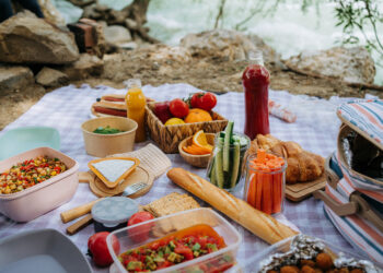 Colourful picnic spread on a blanket with fresh food and drinks.