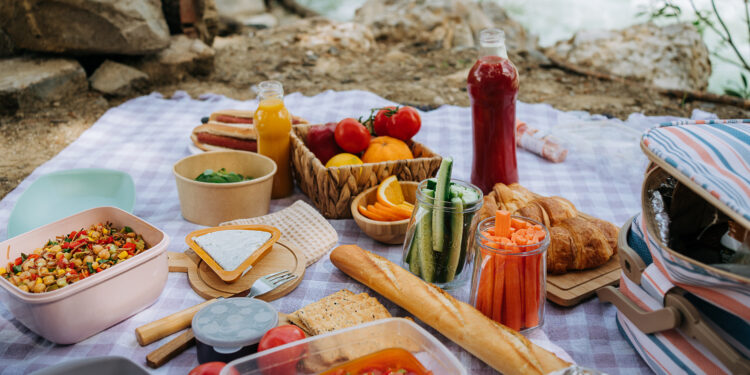 Colourful picnic spread on a blanket with fresh food and drinks.