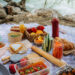 Colourful picnic spread on a blanket with fresh food and drinks.