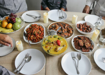 A table set with Caribbean-style curries, fried fish, plant-based sides, and tropical fruit, ready for a shared family meal.