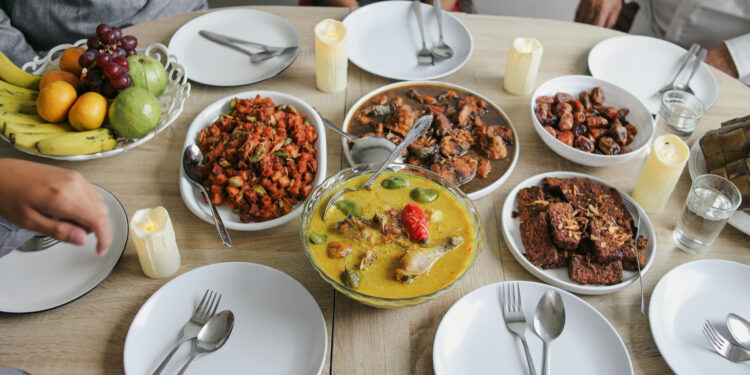 A table set with Caribbean-style curries, fried fish, plant-based sides, and tropical fruit, ready for a shared family meal.