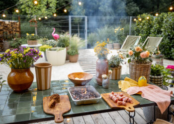 Outdoor garden table set for a barbecue with flowers, food, and summer decor.
