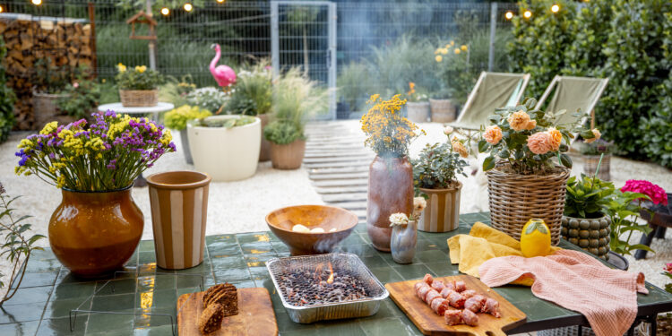 Outdoor garden table set for a barbecue with flowers, food, and summer decor.