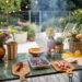 Outdoor garden table set for a barbecue with flowers, food, and summer decor.