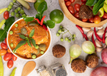 Bowl of red curry with fresh herbs and colourful vegetables.