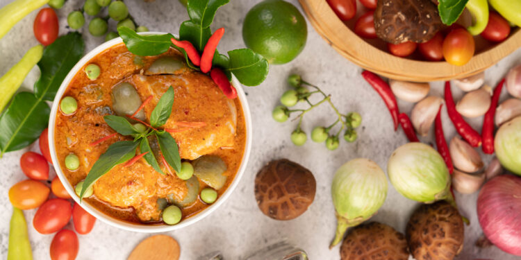 Bowl of red curry with fresh herbs and colourful vegetables.