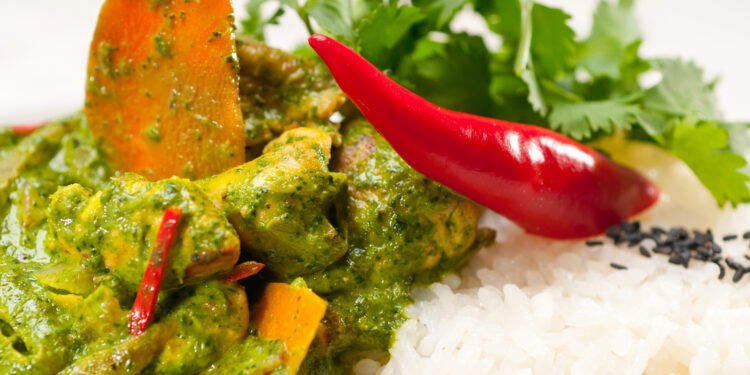 Close-up of Indo-Caribbean curry duck with white rice, red chilli, and coriander garnish