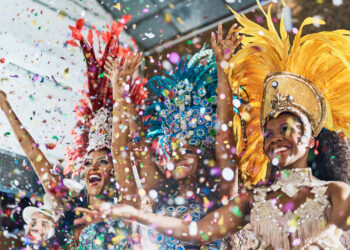 Samba dancers in colourful feathered costumes celebrating at Notting Hill Carnival 2025 with confetti in the air.