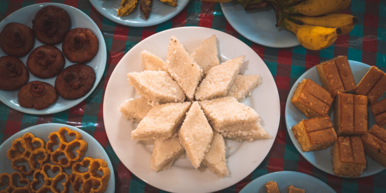 Assorted Indian mithai and Caribbean desserts arranged on plates, including coconut barfi, rum cake, and fried sweets.