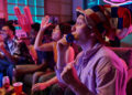 A group of friends enjoying a lively Carnival watch party at home with drinks, snacks, and festive hats.