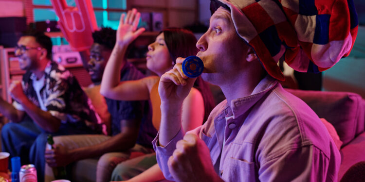 A group of friends enjoying a lively Carnival watch party at home with drinks, snacks, and festive hats.