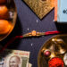 Traditional Raksha Bandhan items arranged on a dark background, including a red rakhi, Indian sweets (motichoor laddoos), a 500 rupee note, a golden thali with diya, rice, kumkum, and roli.