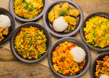 Assorted Indo-Caribbean fusion dishes served with rice on rustic wooden table