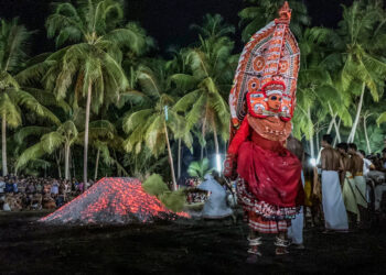 A traditional Theyyam performer in elaborate red costume and headgear during a night-time ritual, symbolising the preservation of ancestral heritage.
