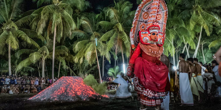 A traditional Theyyam performer in elaborate red costume and headgear during a night-time ritual, symbolising the preservation of ancestral heritage.