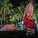 A traditional Theyyam performer in elaborate red costume and headgear during a night-time ritual, symbolising the preservation of ancestral heritage.