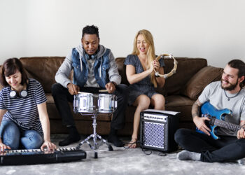 Musicians jamming with keyboard, drum, tambourine, and electric guitar in a cosy living room.