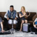 Musicians jamming with keyboard, drum, tambourine, and electric guitar in a cosy living room.