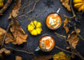 Two mugs of creamy pumpkin soup with thyme garnish surrounded by autumn leaves, gourds, and rustic branches — perfect for Indo-Caribbean autumn warmers.