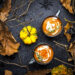 Two mugs of creamy pumpkin soup with thyme garnish surrounded by autumn leaves, gourds, and rustic branches — perfect for Indo-Caribbean autumn warmers.