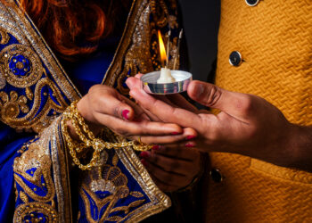 Close-up of a couple holding a lit diya during Karva Chauth celebrations, symbolising love, devotion, and tradition.