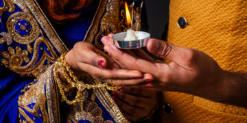 Close-up of a couple holding a lit diya during Karva Chauth celebrations, symbolising love, devotion, and tradition.
