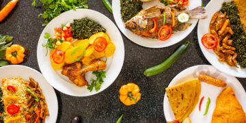 Plates of vibrant Afro-Caribbean and Indo-Caribbean dishes with rice, fried fish, chicken, curries, roti, and fresh vegetables, arranged on a dark table.