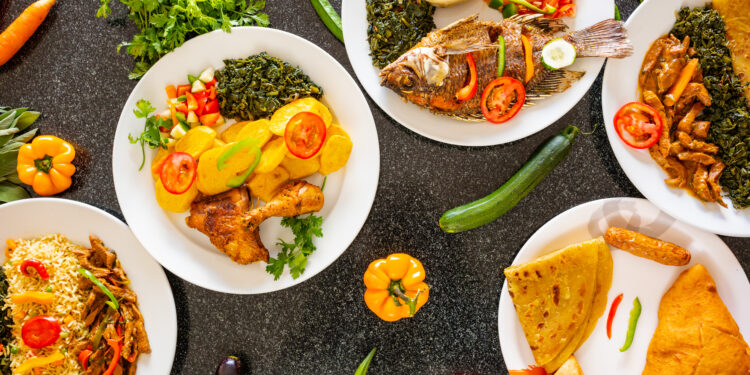 Plates of vibrant Afro-Caribbean and Indo-Caribbean dishes with rice, fried fish, chicken, curries, roti, and fresh vegetables, arranged on a dark table.