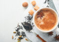 A steaming cup of spiced Indian chai alongside a traditional Caribbean cocoa tea, with cinnamon sticks, nutmeg, and cardamom scattered on the table.