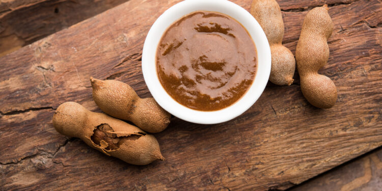 A close-up of tangy tamarind chutney in a bowl, surrounded by Indian samosas and Caribbean pholourie, highlighting the fusion of flavours across continents.
