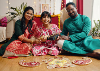 A UK Indo-Caribbean family cooking together in a warm kitchen, passing down traditional recipes like roti and dhal while children watch and help.