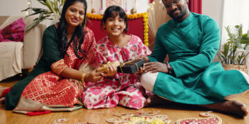 A UK Indo-Caribbean family cooking together in a warm kitchen, passing down traditional recipes like roti and dhal while children watch and help.