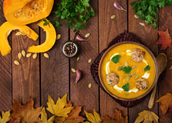 A vibrant Indo-Caribbean pumpkin curry simmering in a cast-iron pot, surrounded by fresh herbs, spices, and golden autumn leaves — celebrating seasonal cooking with Caribbean warmth.