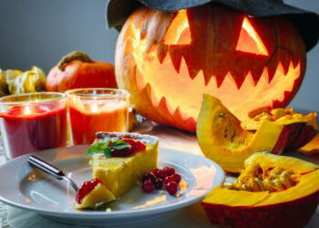 A festive Indo-Caribbean Halloween scene featuring carved calabashes, glowing diyas, and a pot of pumpkin curry surrounded by tassa drums and colourful decorations.