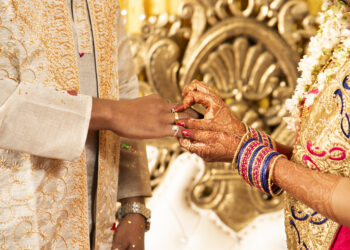 A vibrant Indo-Caribbean wedding in the UK, featuring a couple beneath a mandap decorated with marigolds and tropical flowers, surrounded by guests in colourful attire blending Indian and Caribbean styles.
