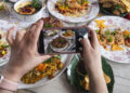 Indo-Caribbean home kitchen scene with hands cooking curry while a phone records a food reel for social media.