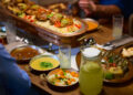 Indo-Caribbean family preparing traditional vegetarian dishes together during a religious ceremony in a home kitchen.