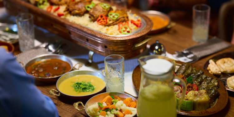 Indo-Caribbean family preparing traditional vegetarian dishes together during a religious ceremony in a home kitchen.