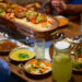 Indo-Caribbean family preparing traditional vegetarian dishes together during a religious ceremony in a home kitchen.
