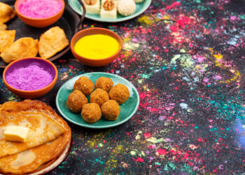 A cosy Lohri party celebration in the UK with family and friends gathered around a small fire pit, wearing colourful Punjabi attire and enjoying traditional food.