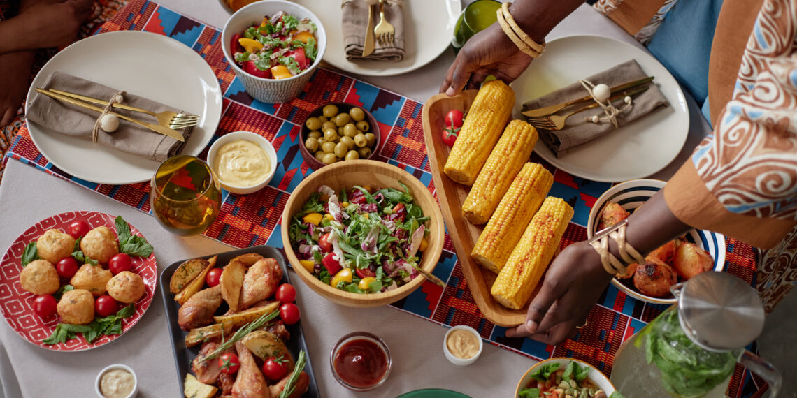 Indo-Caribbean style family table with corn on the cob, fresh salads, fried snacks and colourful place settings