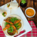 Caribbean-style roti wrap filled with spiced chicken, green beans and grilled aubergine on a white board with dipping sauce