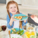 Smiling young girl with braided hair holding a plate with a slice of pie while sitting at a family dinner table with salad, juice, and infused water.